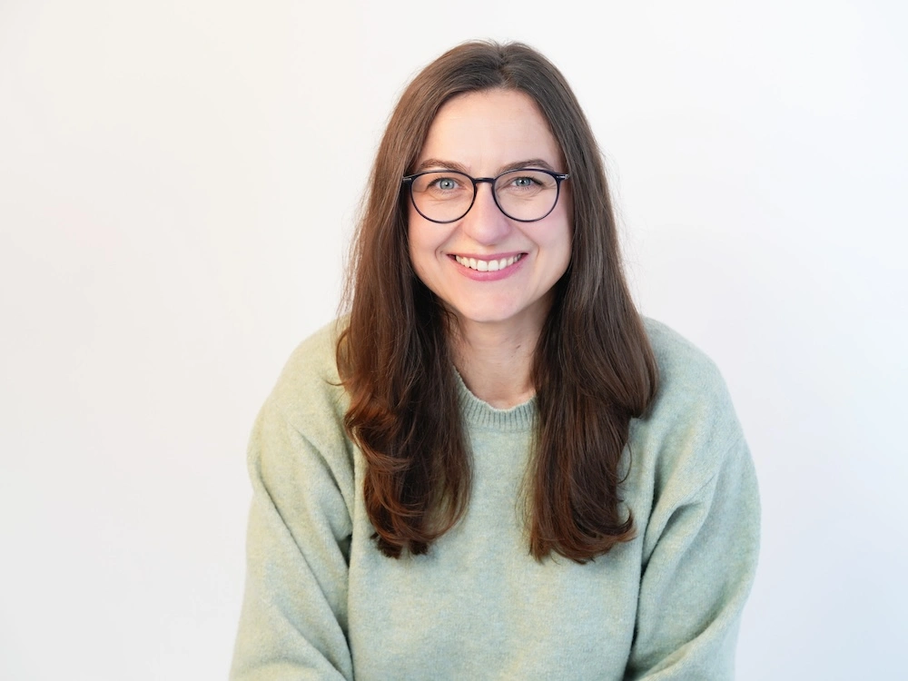 Christine Schreiber sitzt in hellem Pullover vor weißem Hintergrund und schaut freundlich in die Kamera